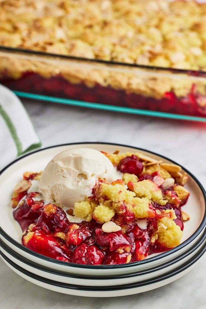 A stack of plates with the top plate holding a serving of cherry dump cake.