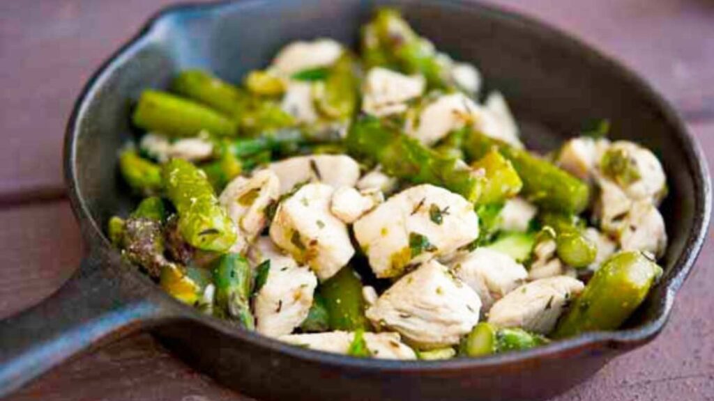 A cast iron skillet filled with chicken and asparagus.