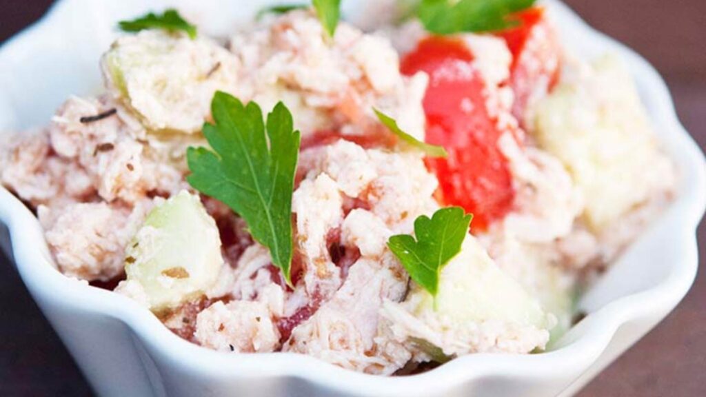 A closeup of a white bowl filled with Chicken And Cucumber Salad.