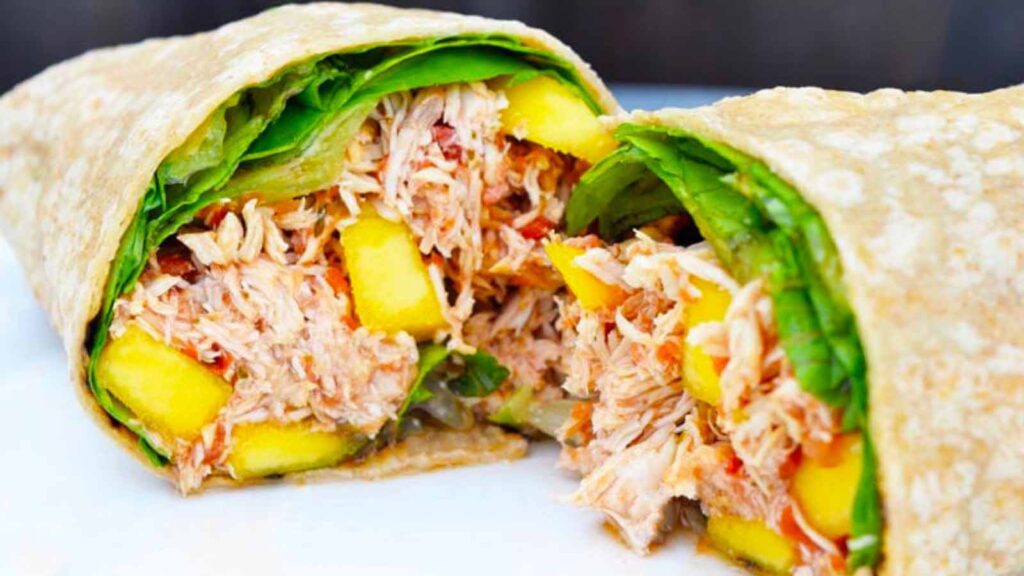 A mango chicken wrap, cut in half and placed on a white plate.