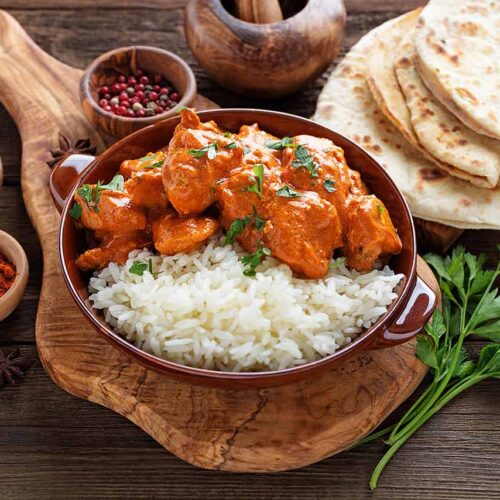 A bowl of chicken tikka masala served with rice, sitting on a cutting board.