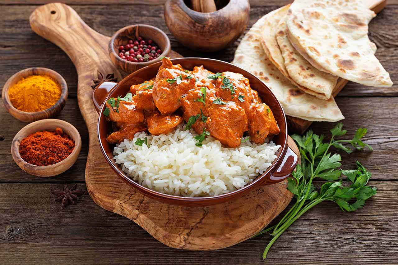 A bowl of chicken tikka masala served with rice, sitting on a cutting board.