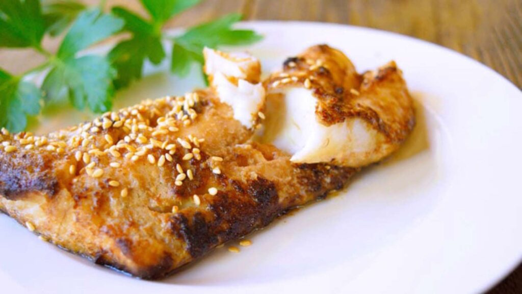 A cod filet on a white plate garnished with sesame seeds.