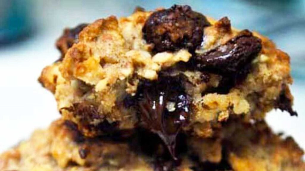 A closeup of a chocolate chip cookie with a warm chocolate chip oozing from the side of the cookie.