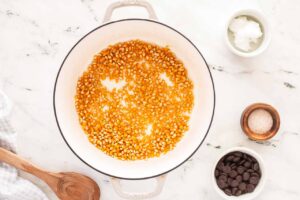 Popcorn kernels in a pot with the remaining three ingredients sitting to the side in small bowls.