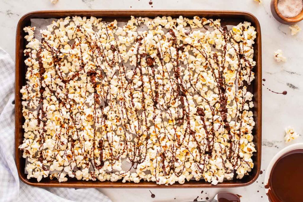 A sheet pan full of popcorn drizzled with melted chocolate.