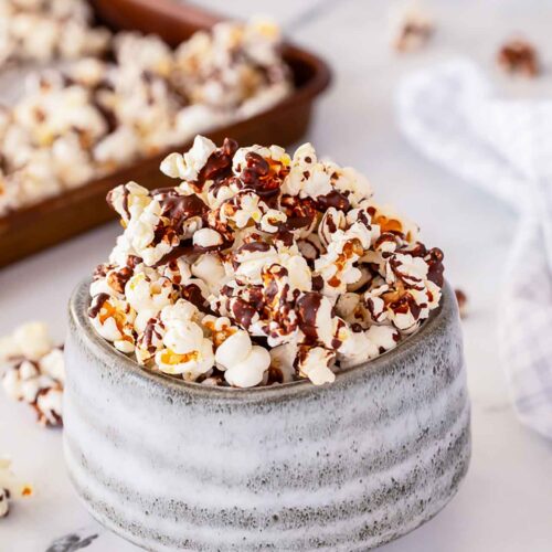 A gray bowl filled with Chocolate Popcorn and drizzled with chocolate.