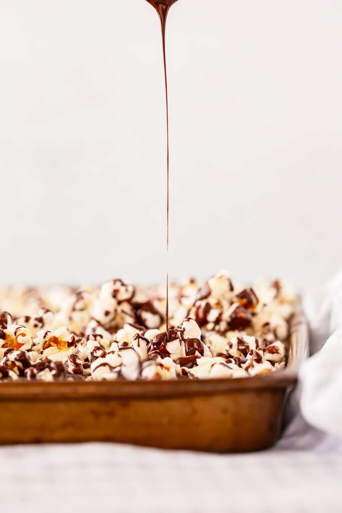 Chocolate being drizzled over a sheet pan full of popcorn.