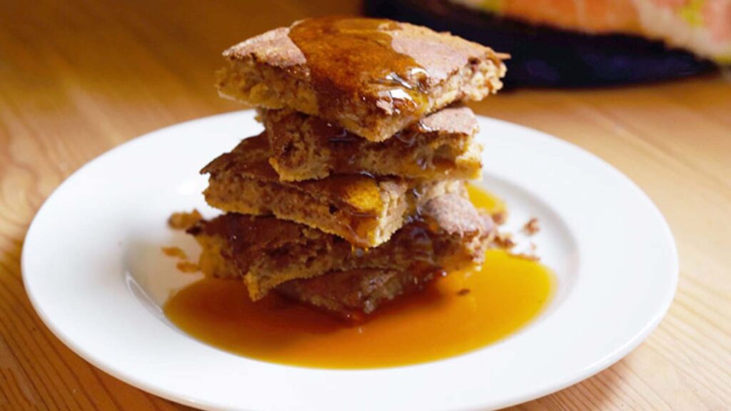 The finished Cinnamon Swirl Pancakes served on a white plate with maple syrup over the top.