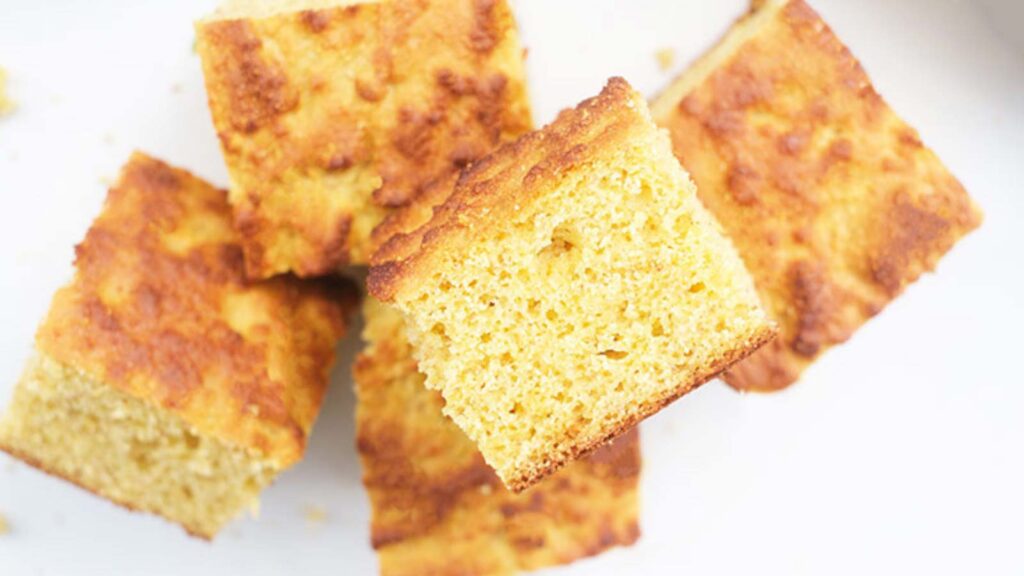 A pile of cut cornbread pieces lay on a white surface.