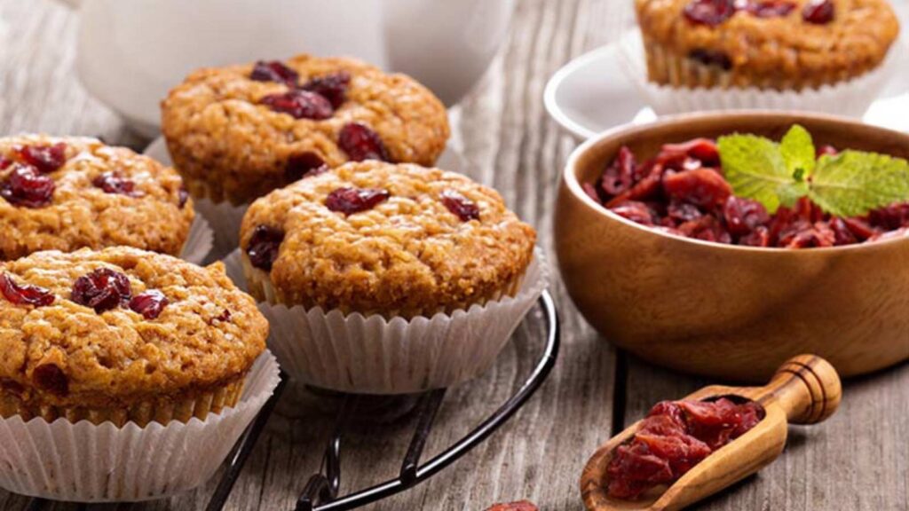 Cranberry Bran Muffins on a wire rack next to a bowl of dried cranberries.