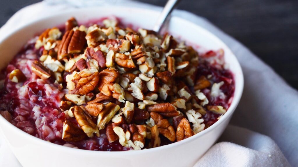 A white bowl filled with cranberry oatmeal topped with chopped pecans.