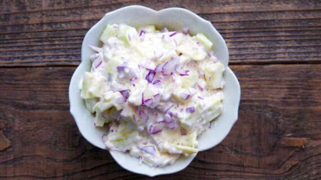 An overhead view of a white bowl filled with Cucumber And Onion Salad.