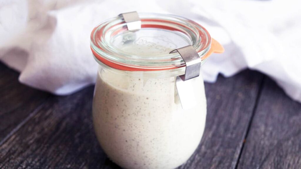 The finished jar of Dairy Free Ranch Dressing sitting on a table next to a white towel.