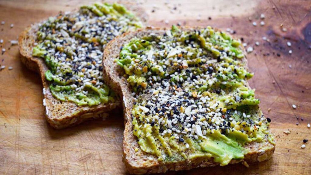 Two slices of Everything Bagel Avocado Toast lay on a wooden surface.