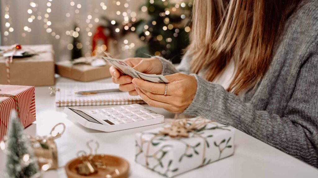 A woman counting cash with a wrapped gift sitting next to her.