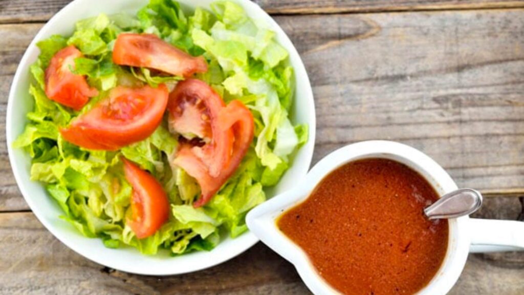 An overhead view of a bowl with a salad in it and a white pitcher next to it filled with French dressing.