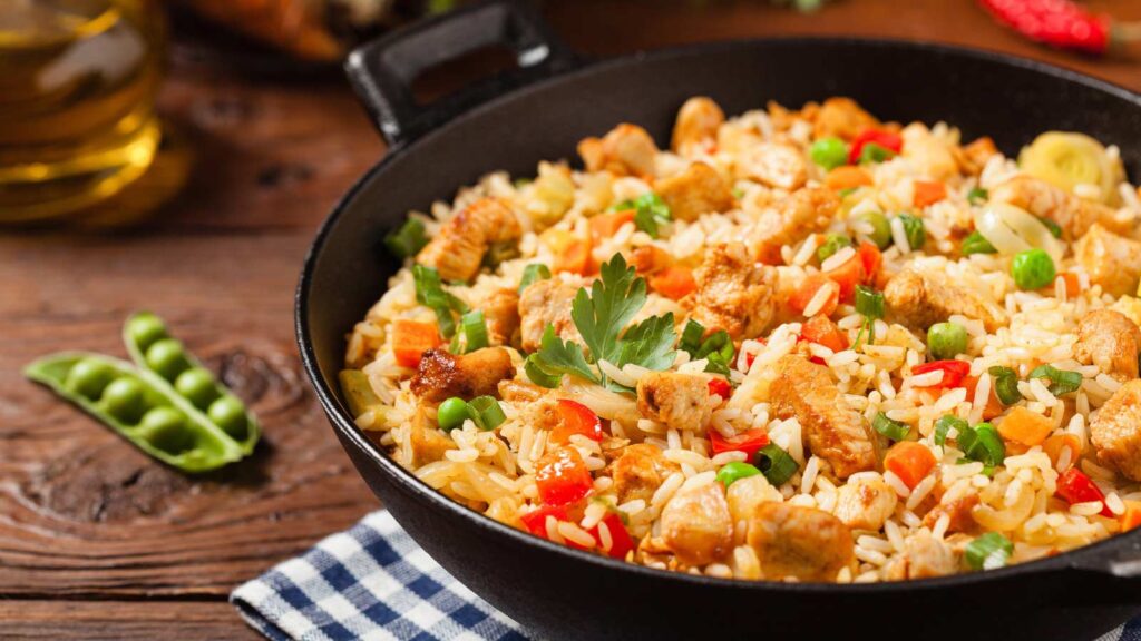 A black skillet filled with chicken fried rice.