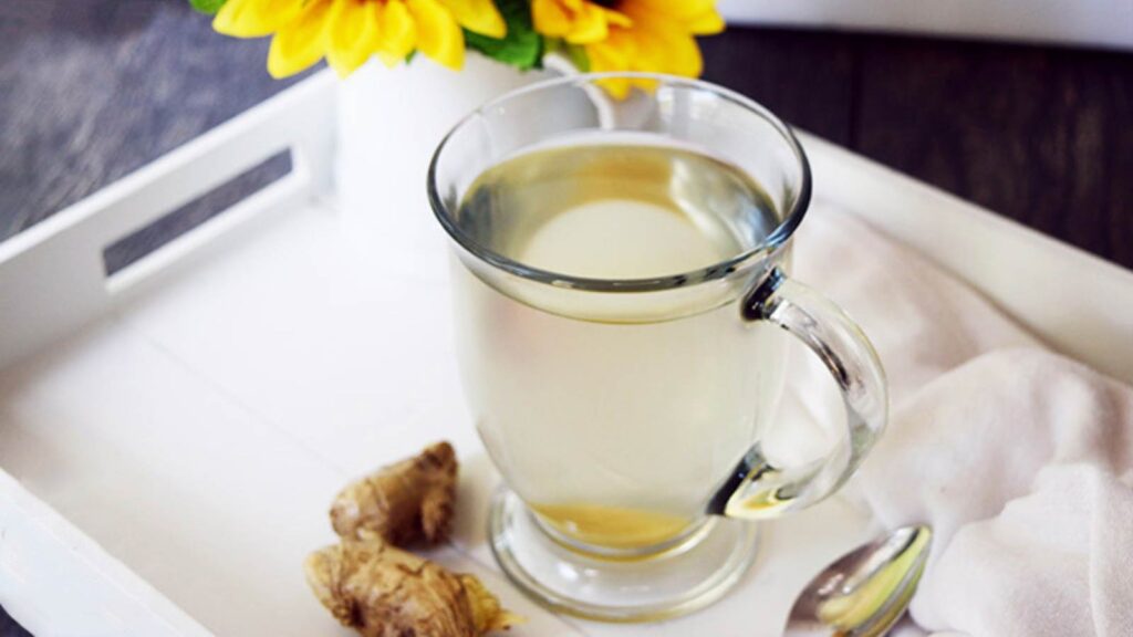 A glass mug filled with Fresh Ginger Tea, sitting on a white serving tray.