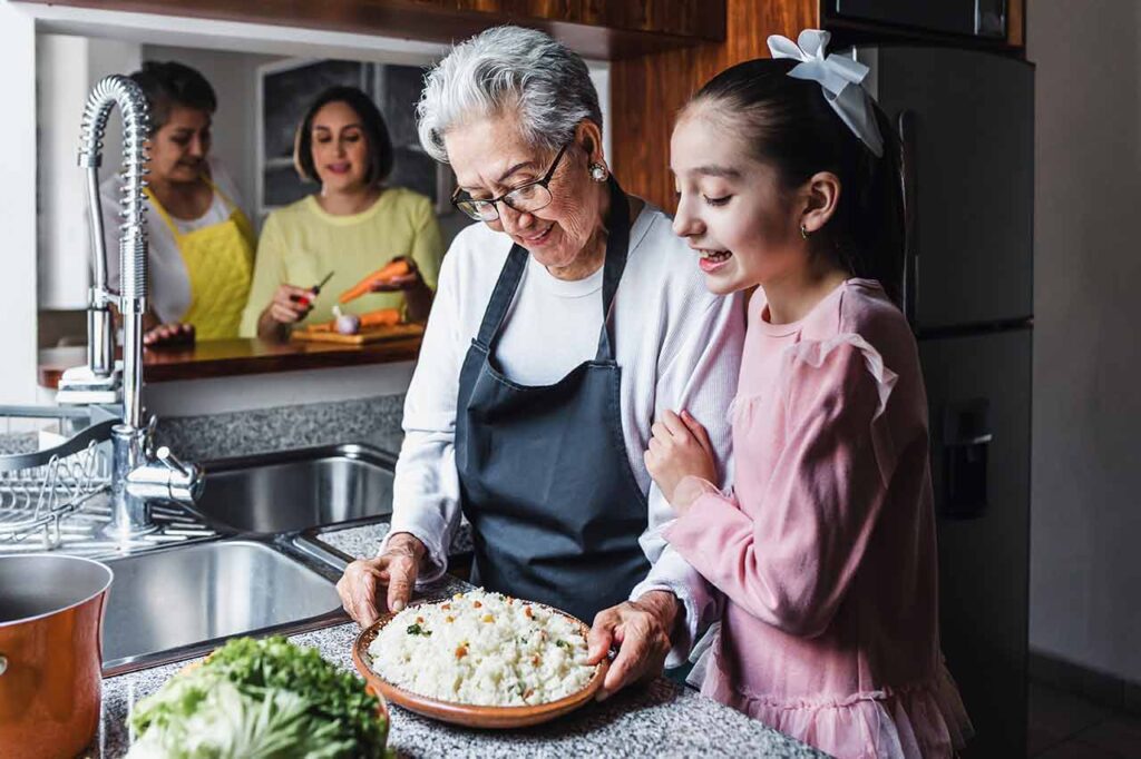 A grandmother looking at a dish of food with her granddaughter.