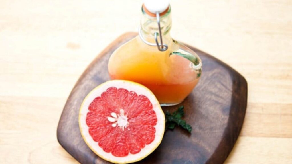 A bottle of Grapefruit Vinaigrette next to half a grapefruit sitting on a cutting board.