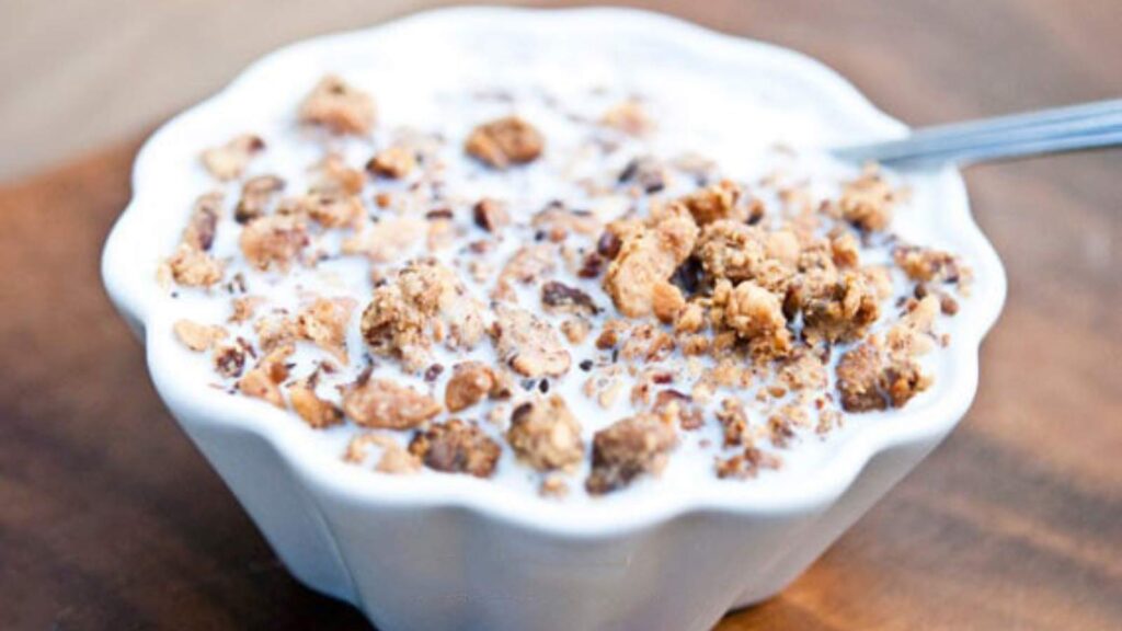 A small, white bowl filled with Copycat Grape Nuts Cereal. A spoon rests in the side of the bowl.