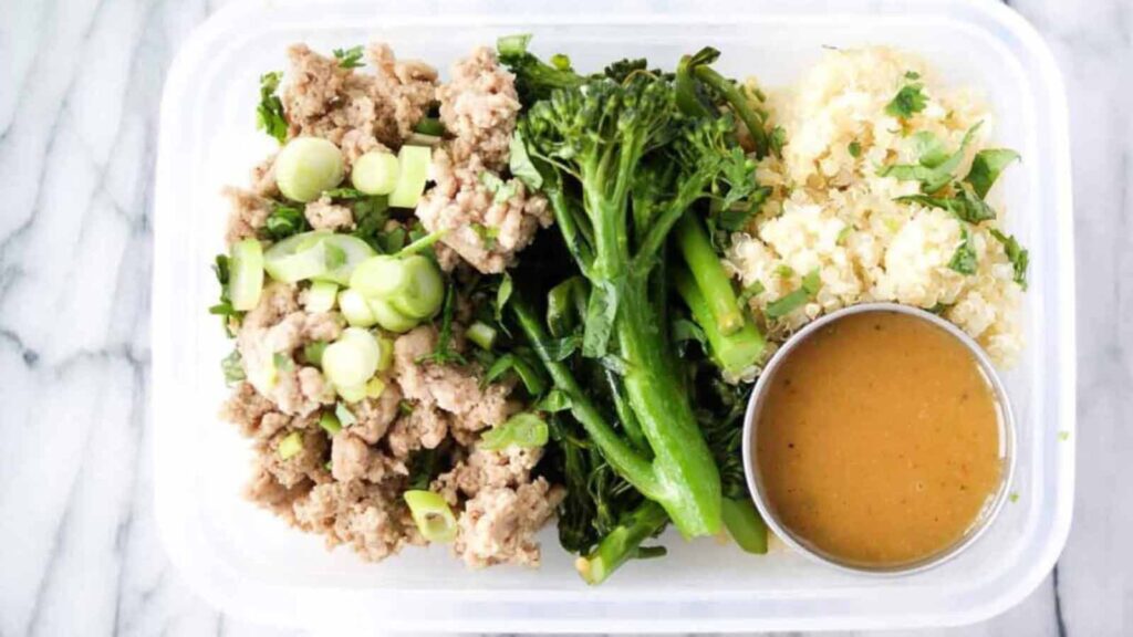 A lunch container filled with ground turkey, broccolini, quinoa and dressing.