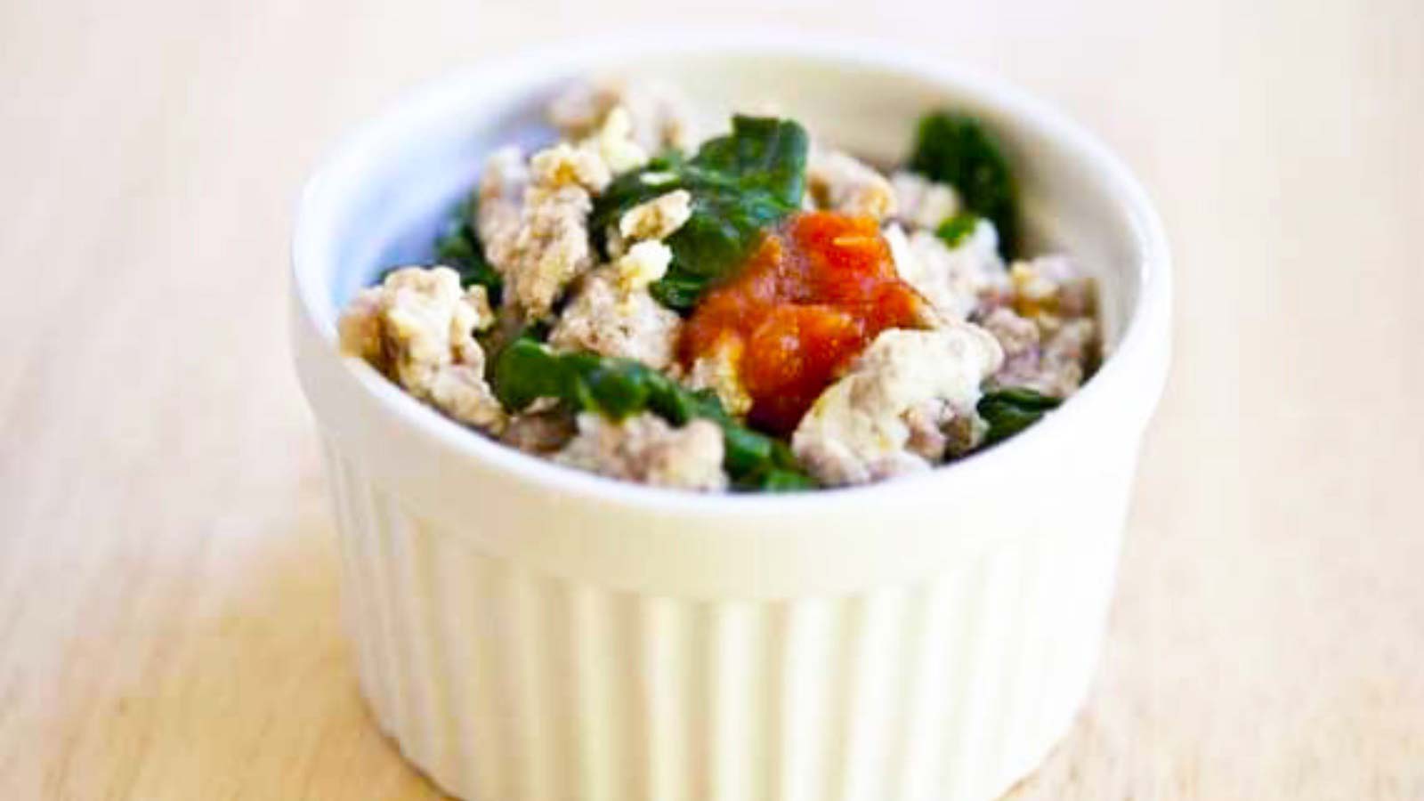 A single, white bowl on a wood background. It's filled with ground turkey scramble.