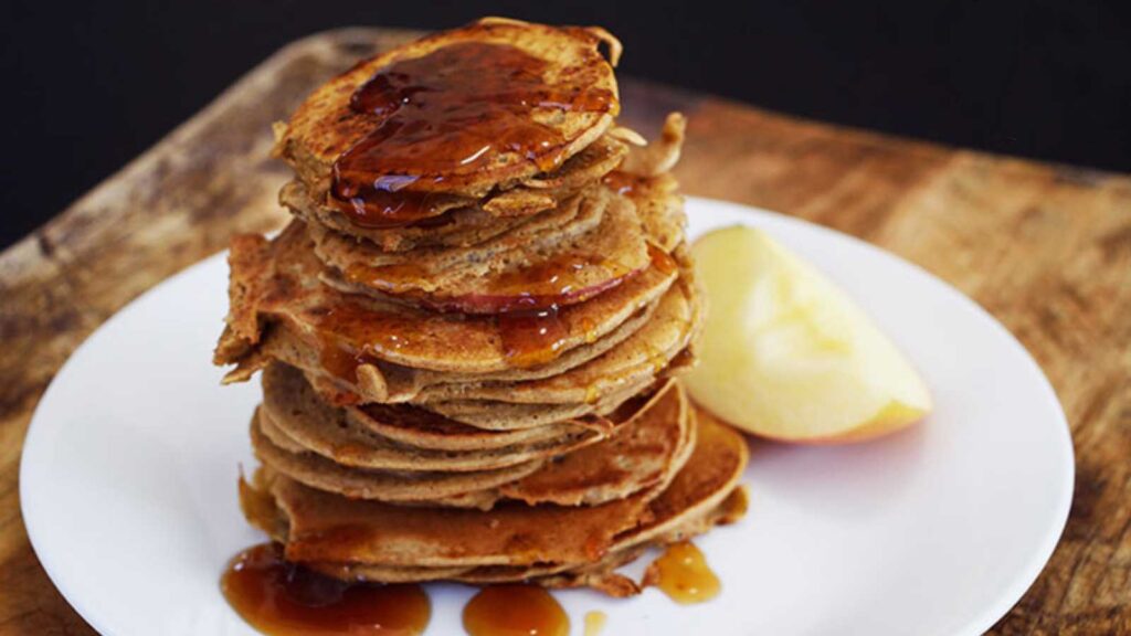 A stack of Healthy Apple Ring Pancakes with maple syrup drizzled over the top.