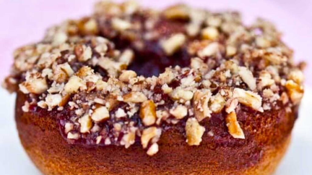 A closeup of a single donut with chopped nuts on top.
