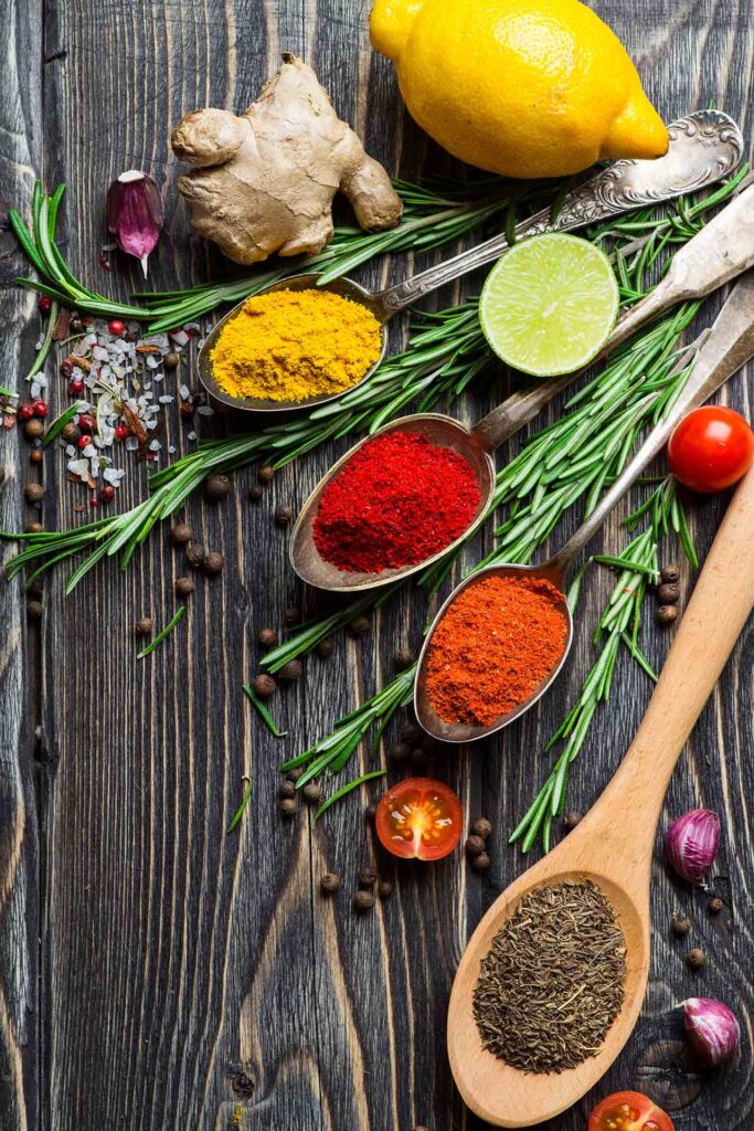 Herbs and spices gathered on a wood surface. Spoons hold dry spices intermingled with fresh herbs.