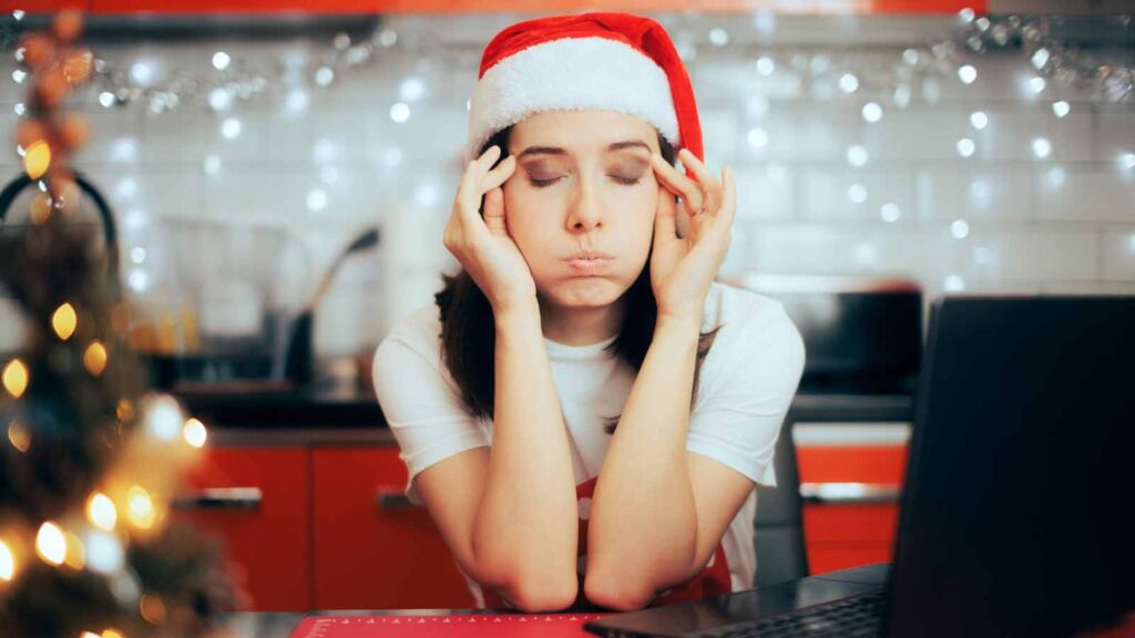 A woman looking stressed sits at a table with eyes closed, wearing a santa hat.