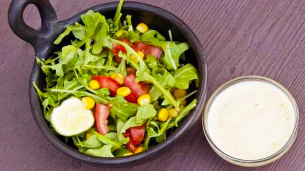A black bowl filled with salad next to a small, glass bowl filled with Honey Lime Vinaigrette.