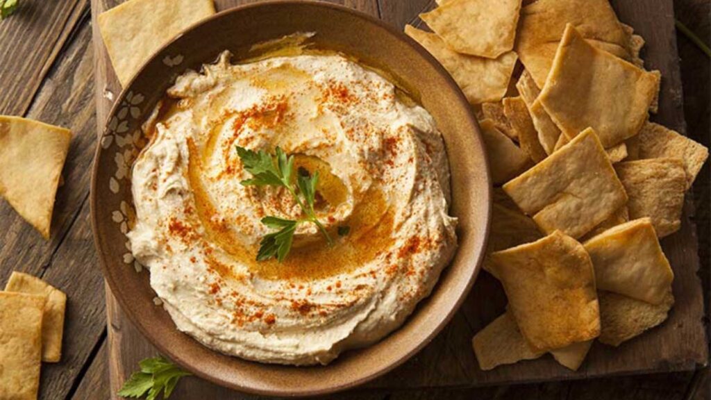 An overhead view of a bowl filled with hummus and surrounded by pita chips.