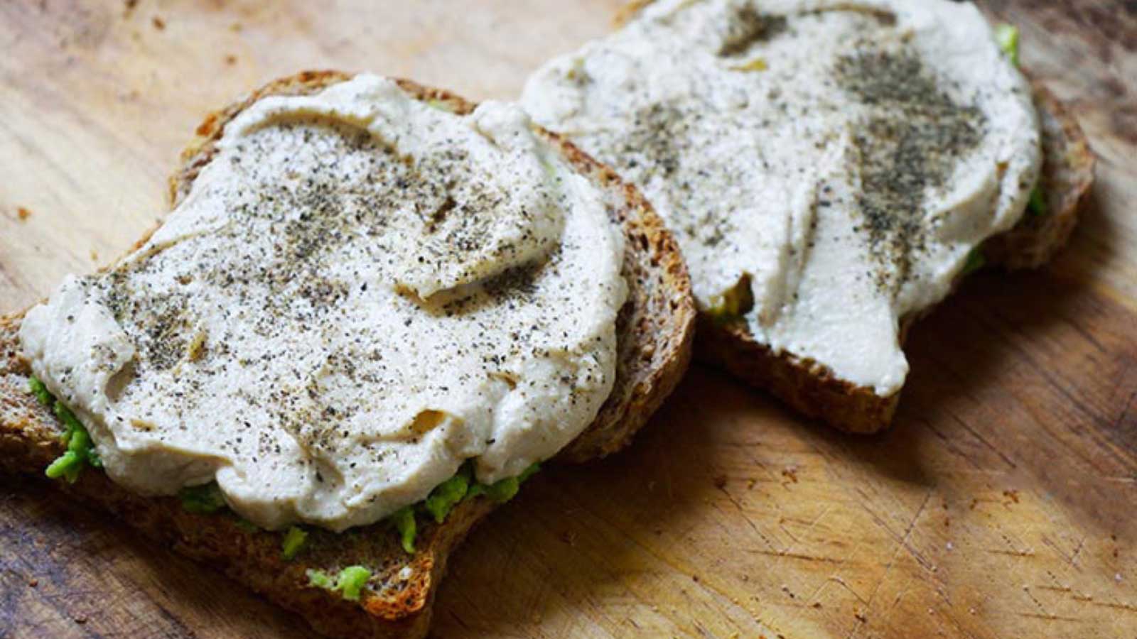 Two slices of Hummus Avocado Toast lay on a cutting board.