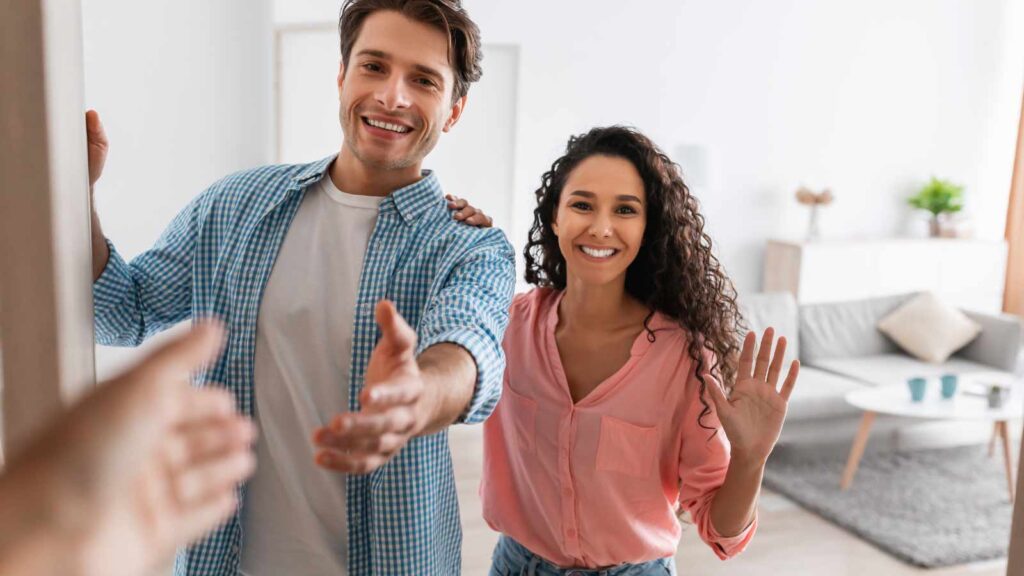 A couple greeting somebody at their door.
