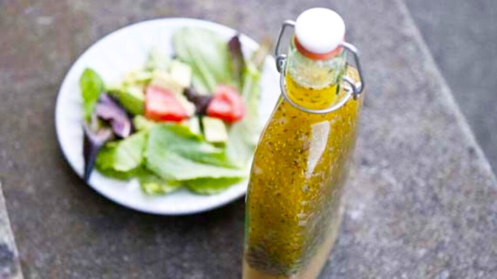 A bottle of homemade Italian dressing sits next to a salad in a white bowl.