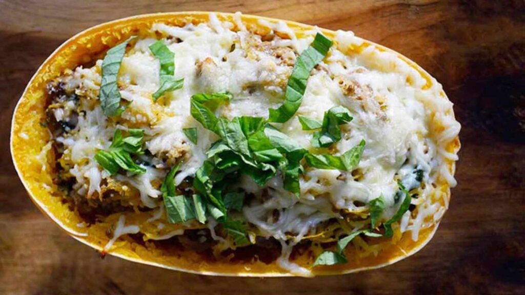 An overhead view of a half of a spaghetti squash stuffed and topped with melted cheese and fresh greens.