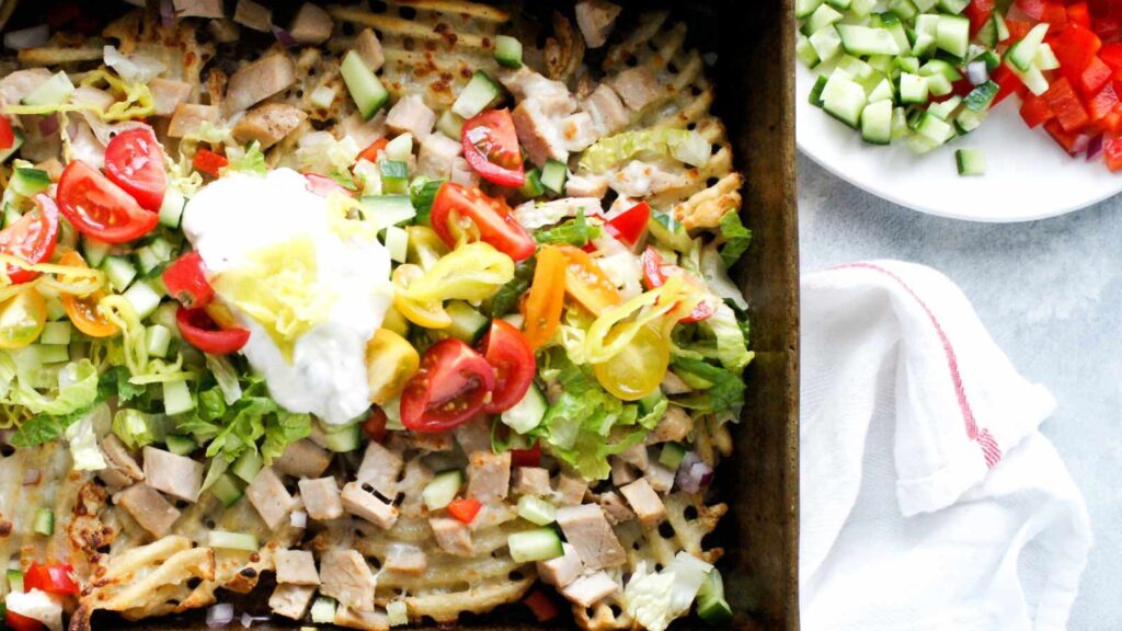 An overhead view of loaded Greek fries on a sheet pan.