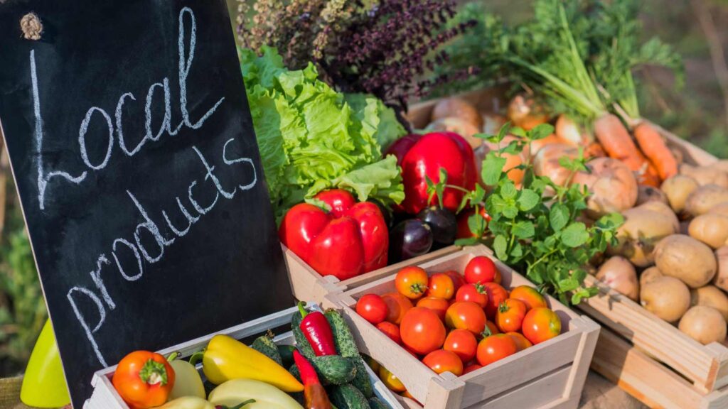 Table with fresh vegetables and a sign of local products