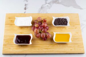 Sauces, chocolate chips and grapes placed on a cutting board.