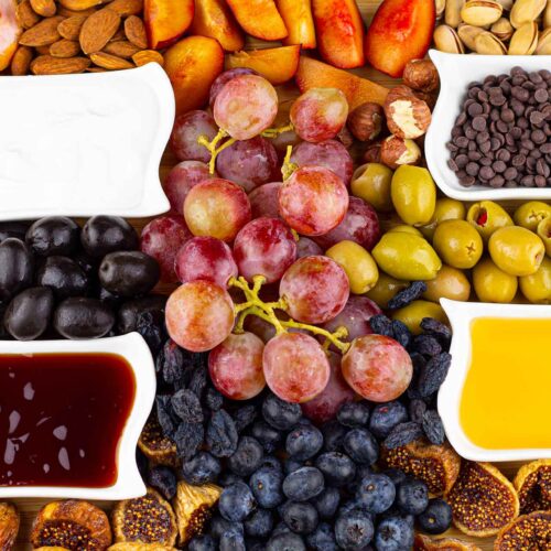 A shot of the middle of a Dessert Mezze Platter which has grapes, four bowls of dip, nuts and fresh fruit as well as olives on it.