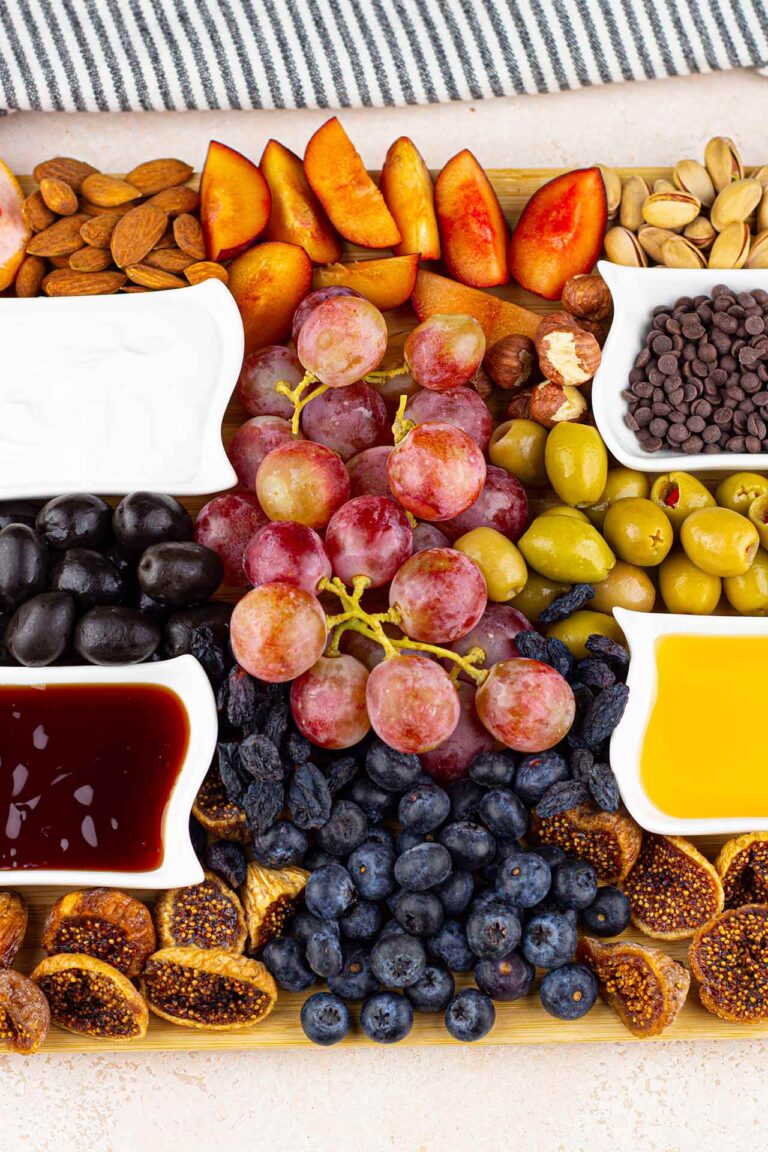 A shot of the middle of a Dessert Mezze Platter which has grapes, four bowls of dip, nuts and fresh fruit as well as olives on it.