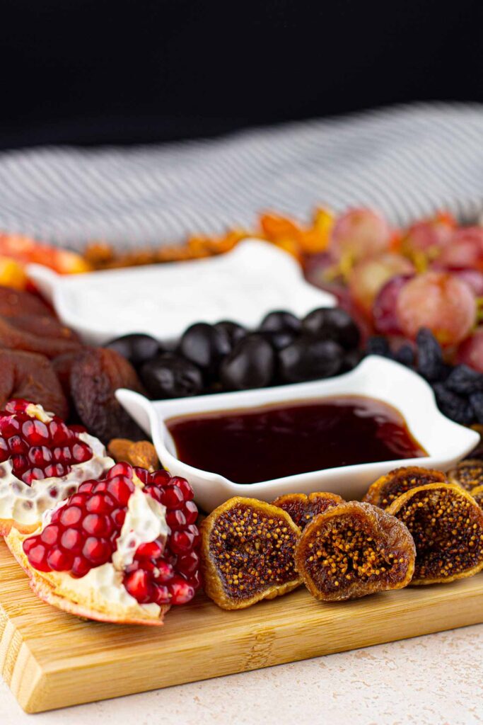 A front view of a Dessert Mezze Platter shows a broken pomegranate, dried figs, olives, and two bowls of dip.