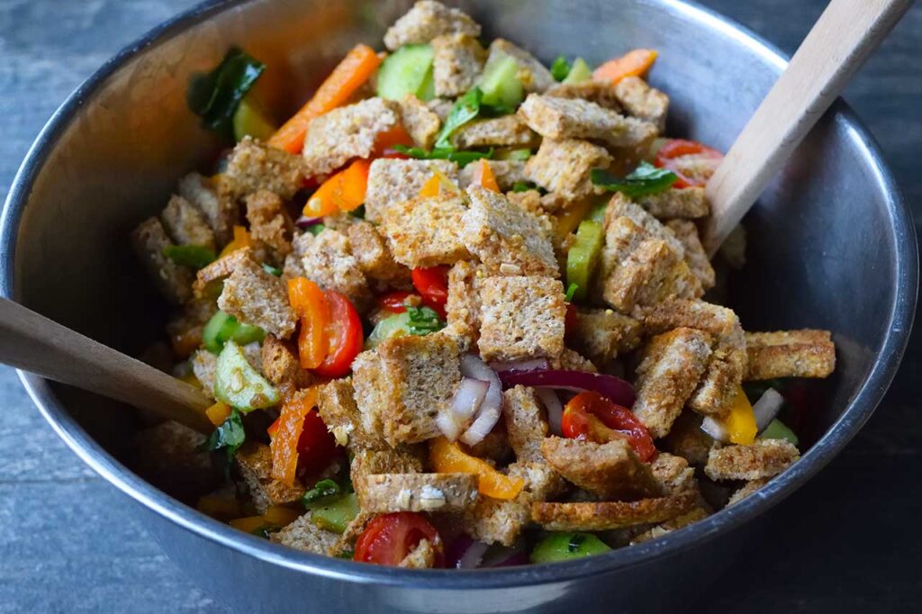 A large metal mixing bowl filled with Panzanella.