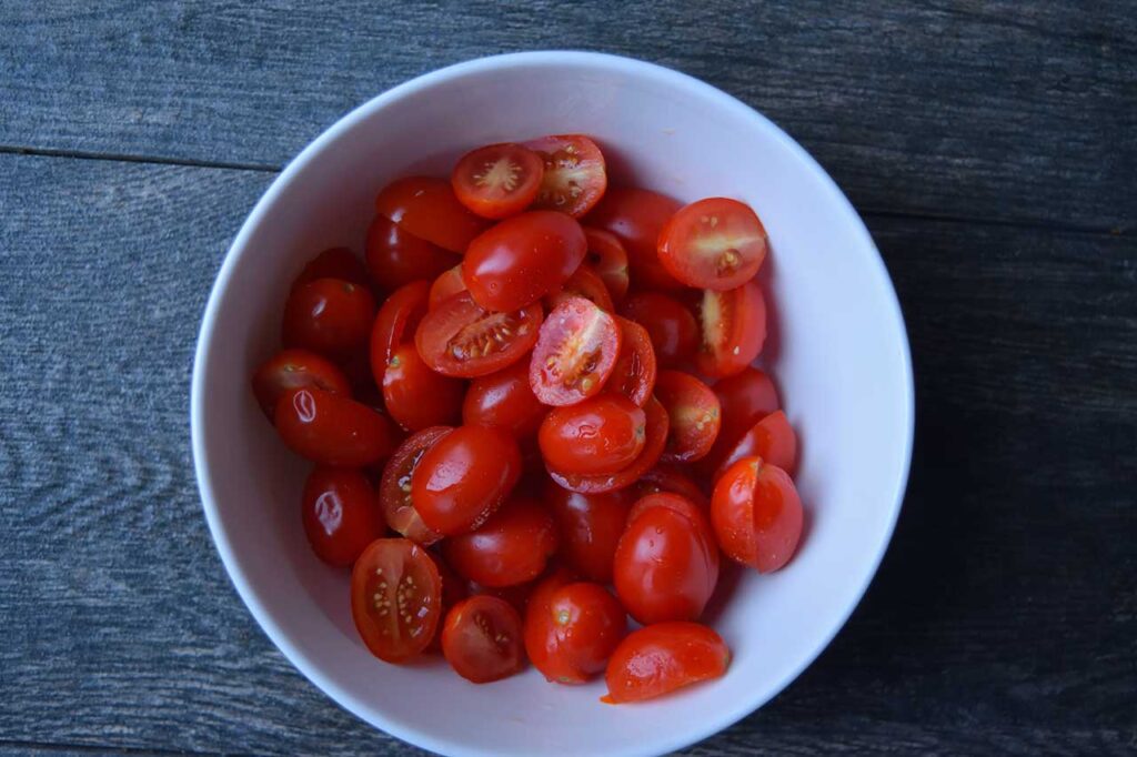 A white bowl filled with halved grape tomatoes.