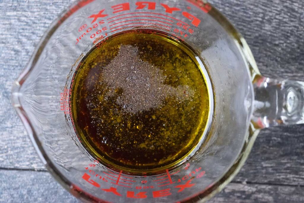 Vinaigrette ingredients poured into a glass measuring cup.