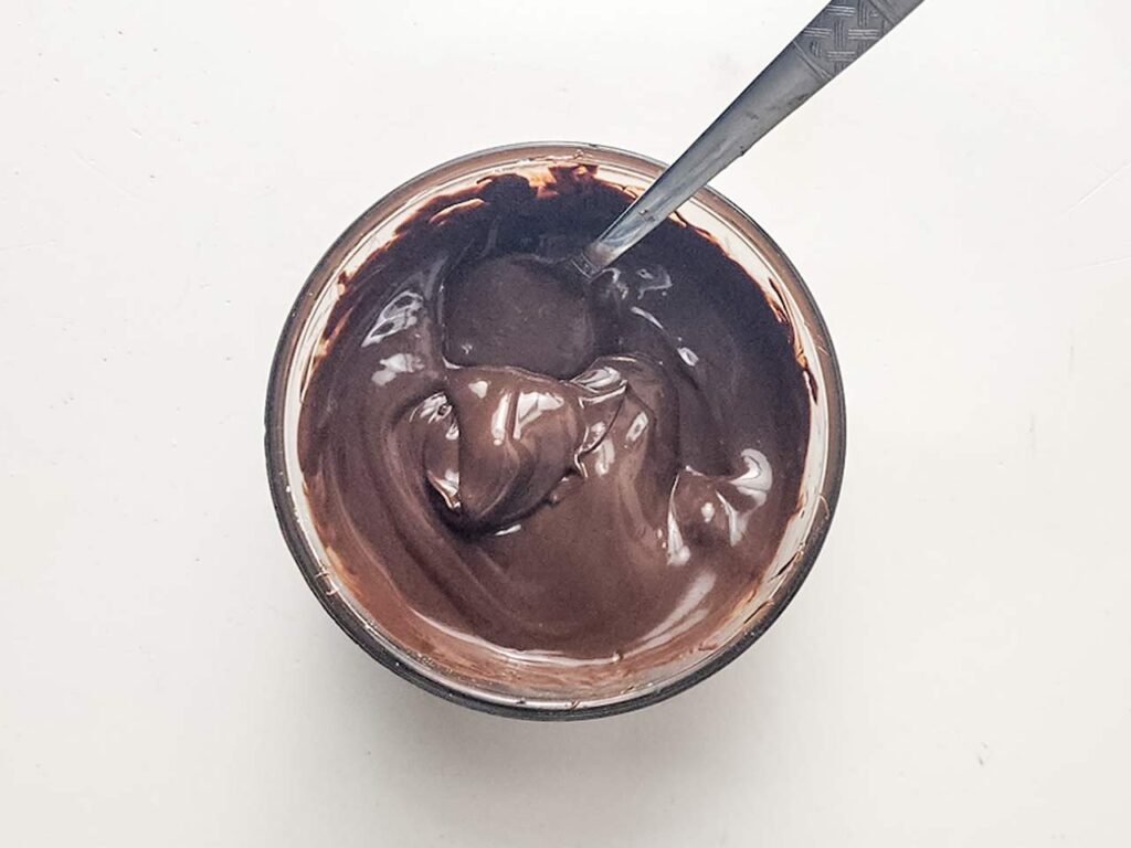 Chocolate chips and coconut oil melted in a small bowl. A spoon rests in the bowl.