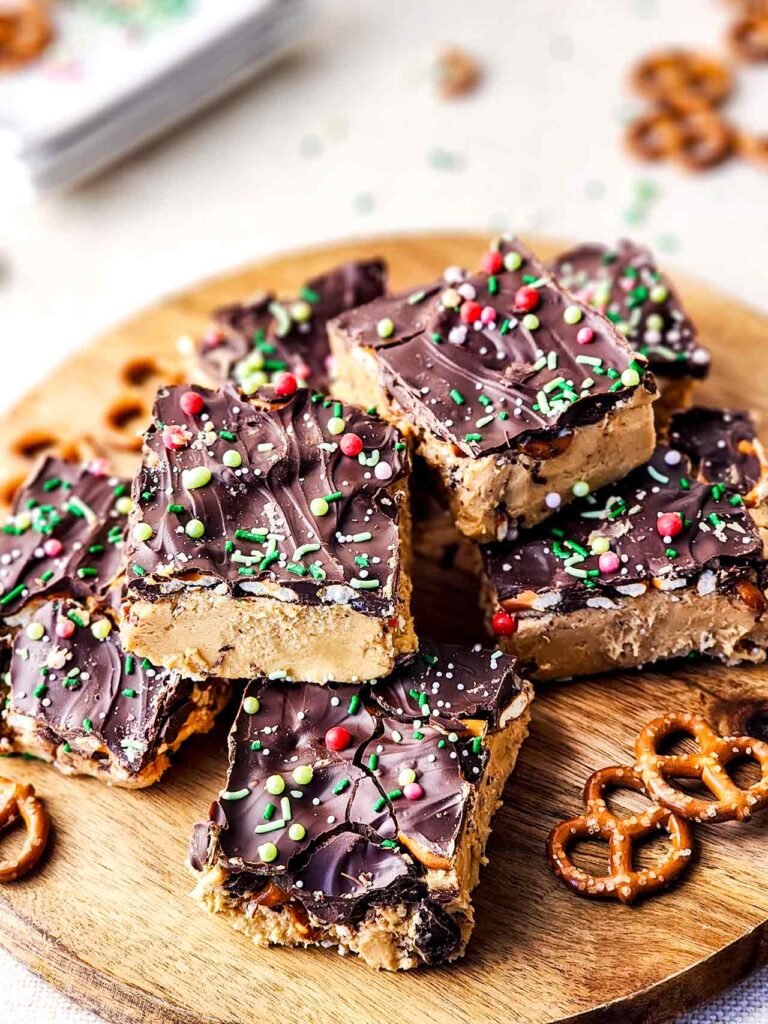 A side view of cut Peanut Butter Chocolate Bars served on a cutting board with a few pretzels.