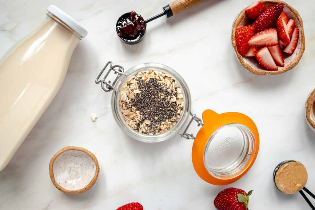 Chia seeds added to overnight oats in a canning jar on a white surface.